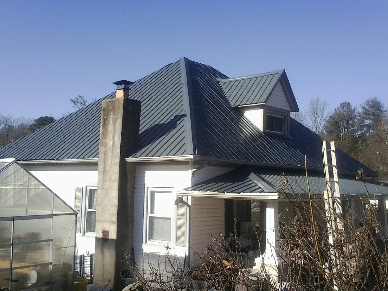Dark blue standing seam metal roof on a white farmhouse with dormer — Slate & Tile Roof Repair by Roofing Brothers in Winooski