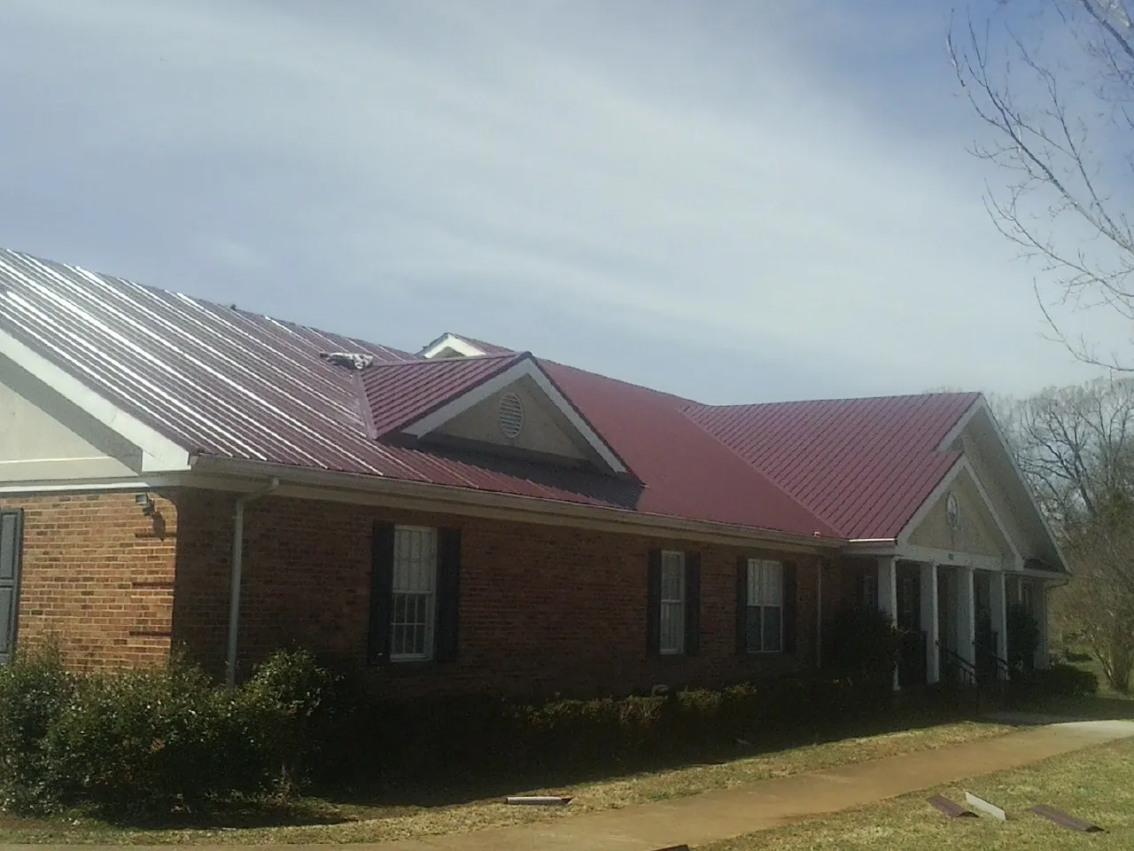 Red metal roof with gabled entries on a long brick building, from a Hail Damage Roof Repair job in Winooski
