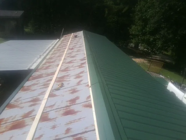 Old rusted panels beside newly installed green metal roofing — Wind Damage Roof Repair by Roofing Brothers in Winooski
