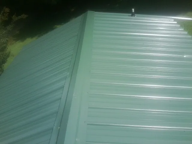 New green metal panels meeting at the ridge of a roof — Flat Roof Repair work by our crew in Winooski