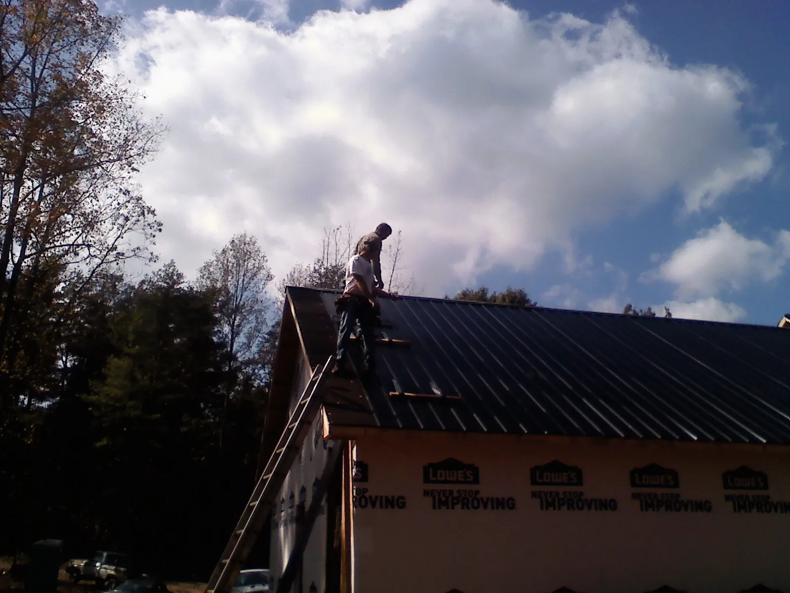 Roofer fastening dark metal panels high against a cloudy sky, from a Roof Inspection job in Winooski