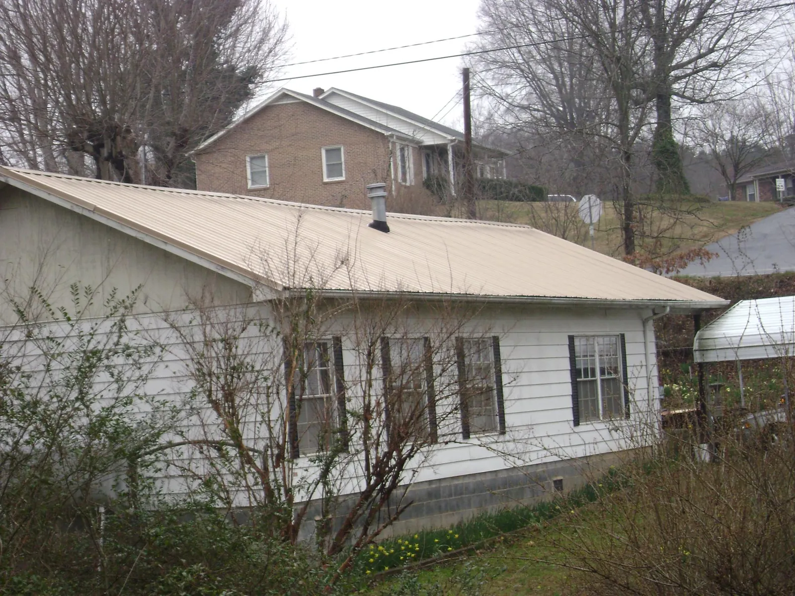 Tan metal roof on a white sided house set into a hillside — Commercial Roofing by Roofing Brothers in Winooski